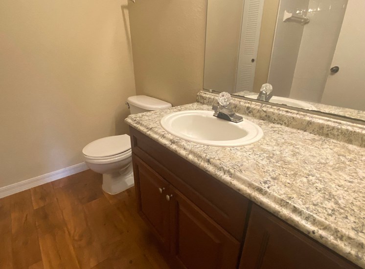 Bathroom with wood floors, extended granite vinyl countertop, mirror, and toilet