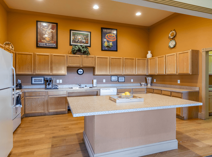 Clubhouse kitchen with wood cabinetry, large island, white appliances and coffee maker with wood style flooring