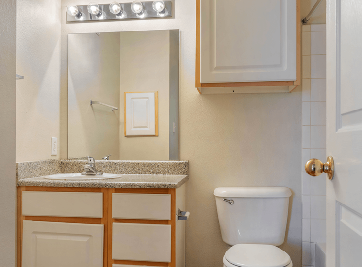 Bathroom with granite inspired countertop, large vanity mirror, two tone cabinetry, toilet and white tile surround