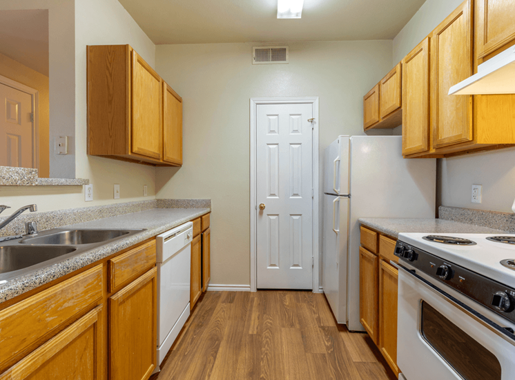 Kitchen with wood cabinetry, wood style flooring, white appliances, double basin sink, pantry door