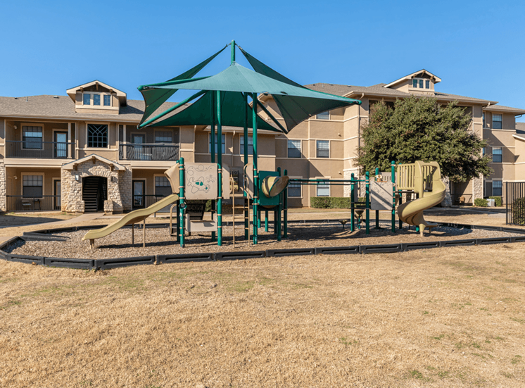 Outdoor playground with slides surrounded by building exterior and native landscape