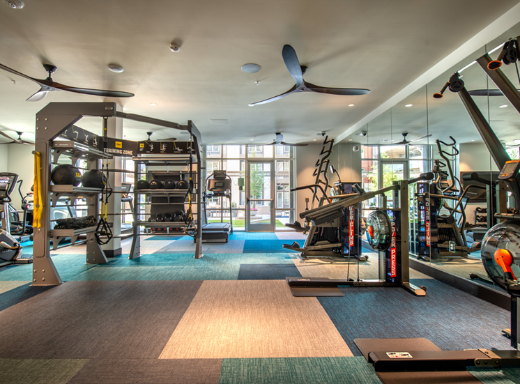 Fitness center with cardio and strength machines, ceiling fans and large mirror wall