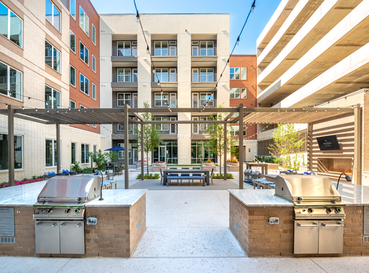 Outdoor grill area in courtyard with gas grills, pergola, hanging lights and alfresco dining