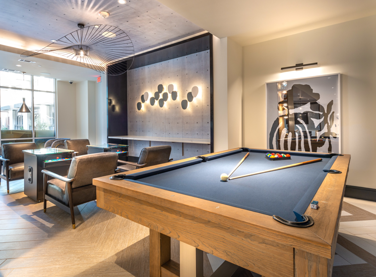 Clubhouse game room with pool table, arcades, unique haning ceiling art and lighted accent wall and countertop
