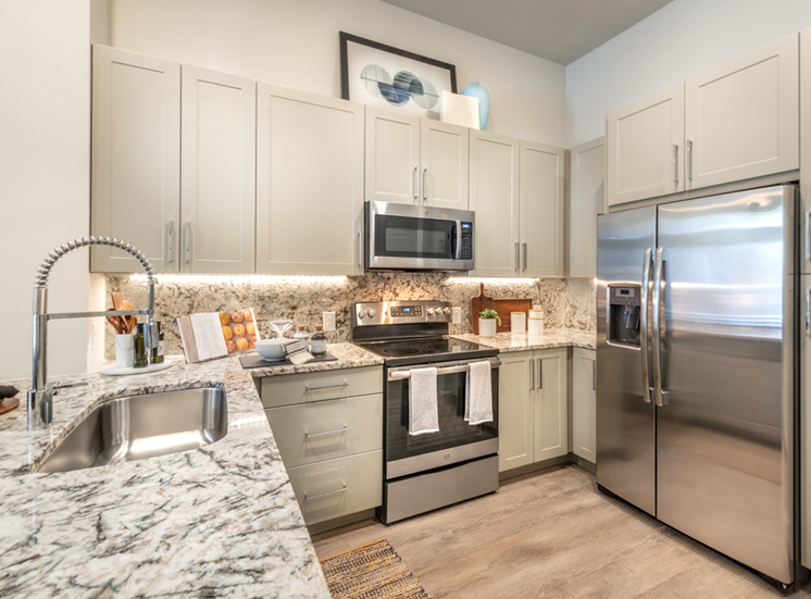 Staged kitchen with stainless appliances, granite countertops, goose neck faucet, taupe shaker cabinets, glass top stove and wood style flooring