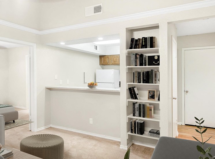 View of kitchen from the living room. White appliances and brown cabinets with crown molding trim. Built in bookshelf in living room staged with books and décor.