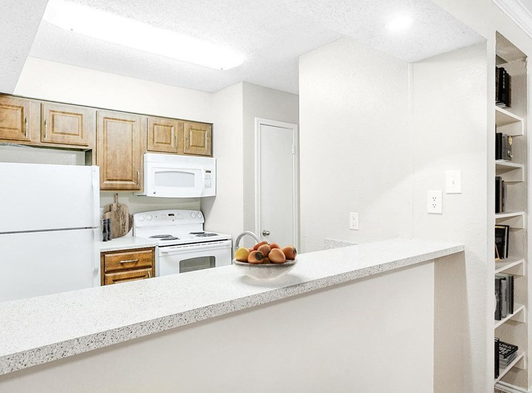 Double basin sink with white appliances, brown cabinets and view of pantry. Built in book case can be seen in front of the kitchen.
