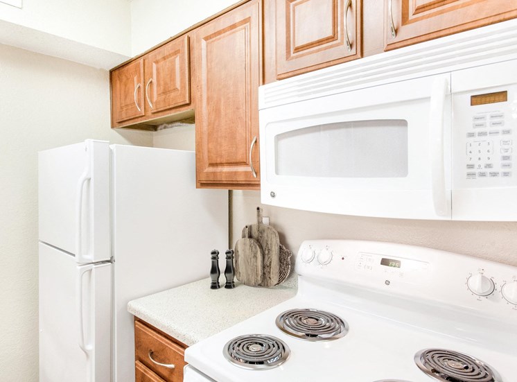 View of white fridge, electric stove and overhead microwave with brown cabinets.