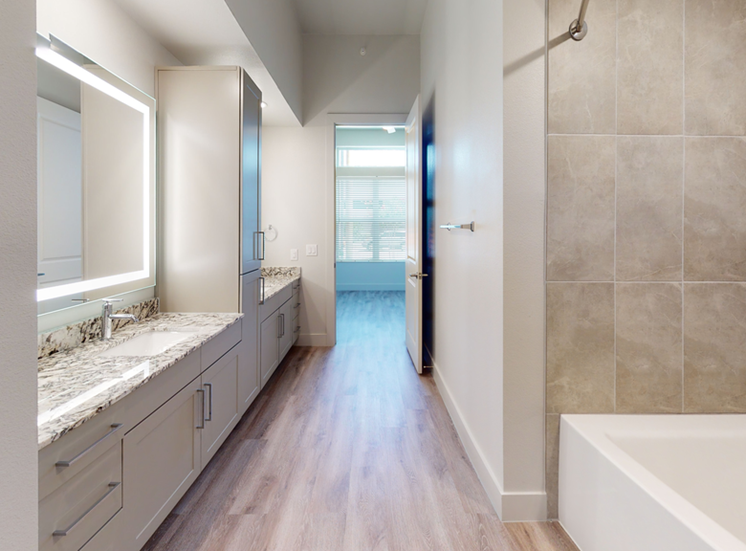 Bathroom with garden tub, wood style flooring, granite countertops, dual vanities, custom vanity mirror and taupe cabinetry