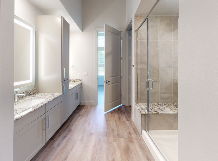 Bathroom with wood style flooring, walk in shower with granite bench, granite countertops, dual vanities, custom vanity mirror and taupe cabinetry