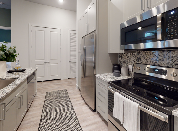 Staged kitchen with granite countertops, stainless appliances, wood style flooring, runner rug, shaker cabinetry and granite backsplash