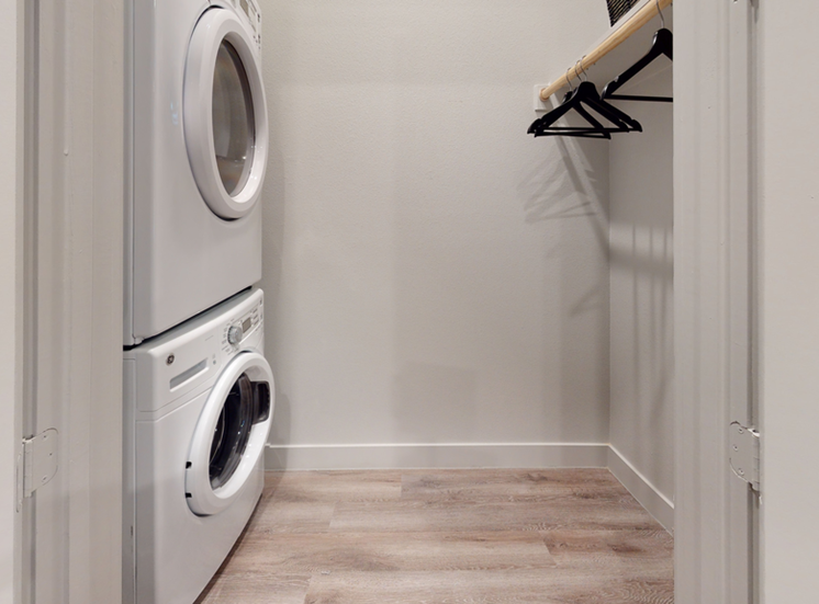 Staged laundry room with stacked front loading washer and dryer with clothes rack and shelf