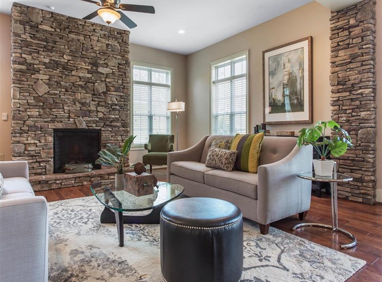 Clubhouse Seating Area with Grey Couches Triangle Glass Coffee Table Brick Fireplace with Windows and Decorations