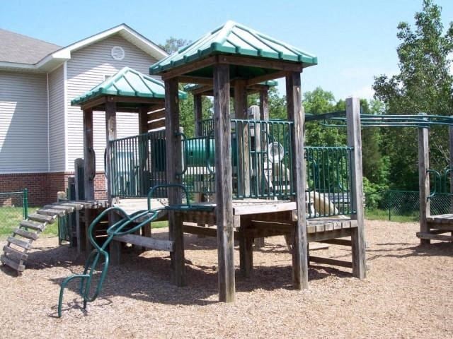 Wooden Playground with Green Accents on Mulch with Building Exterior and Treeline in the Background