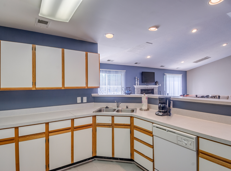 The clubhouse kitchen has a large breakfast bar that opens to the remainder of the clubhouse. The kitchen includes linoleum flooring, white cabinets with tan trim, a double basis sink, a dishwasher and coffee pot.