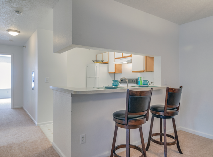 The three bedroom kitchen features a breakfast bar, white cabinets with tan trim, and white appliances. This mini model has two barstools at the breakfast bar.