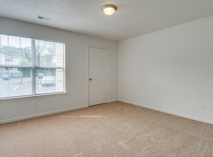 The vacant bedroom has wall to wall carpet, a large picture window and a door leading to a closet.