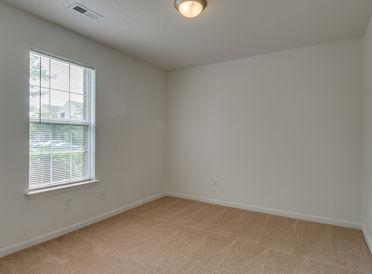 The vacant bedroom has wall to wall carpet, white walls and a standard window on one of the walls.