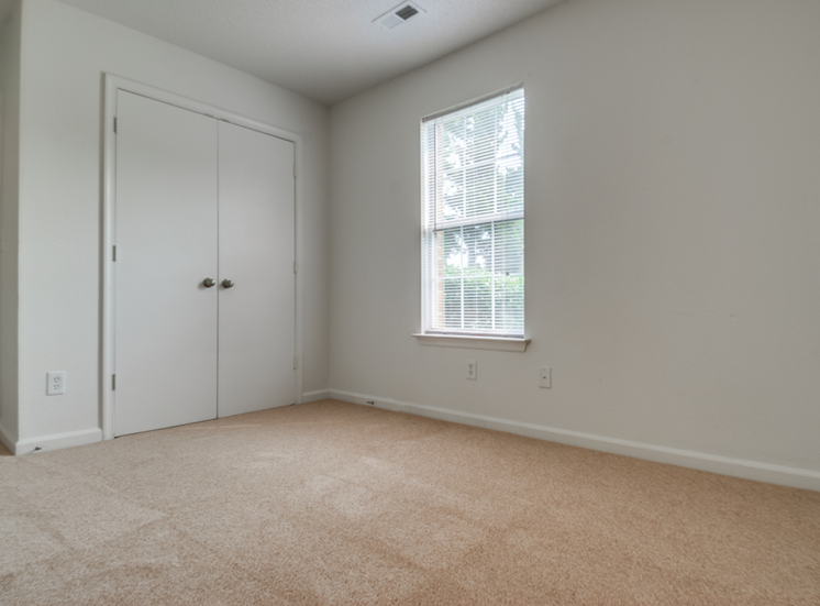 The vacant bedroom has wall to wall carpet, white walls, one standard window, and double doors opening to the closet.