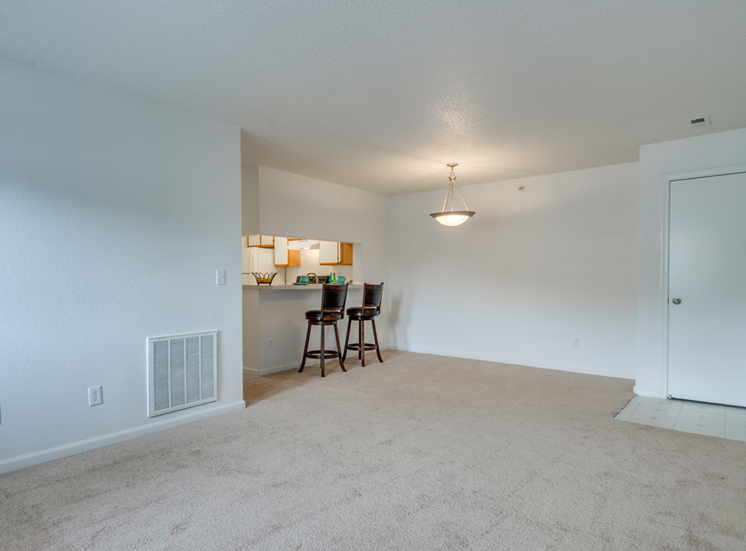 The living and dining room has carpet with linoleum flooring in the entry. There is breakfast bar that opens to the kitchen. This mini model is furnished with two barstools positioned at the breakfast bar.
