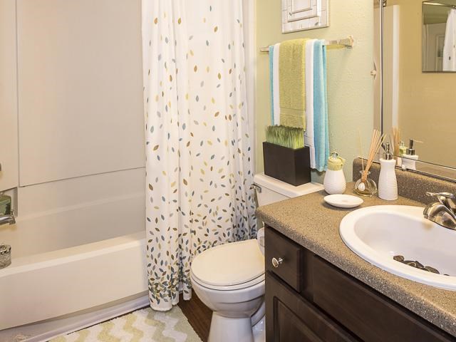 Model Bathroom with White Shower Curtain Brown Cabinets and Tan Counters