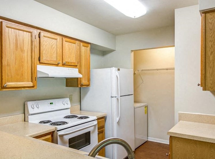 L Shaped Kitchen with Blonde Cabinets Tan Counters and White Appliances and Utility Closet with Washer Visible in the Background