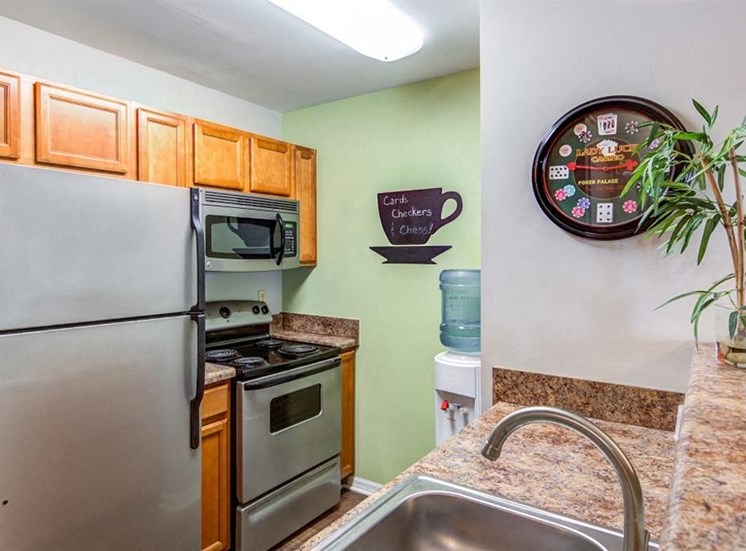 Kitchen with Blonde Cabinets and Stainless Steel Appliances with Beige Counters and Water Cooler Next To Coffee Cup Decoration on the Wall
