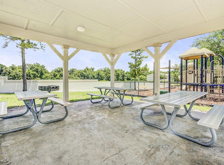 A pergola with three picnic tables and a BBQ grill near the playground.