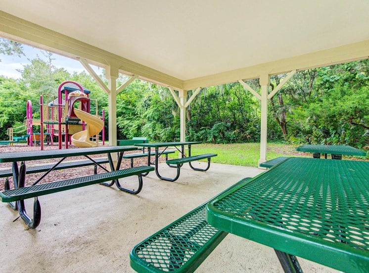 A pergola over 4 picnic tables near the playground equipment.