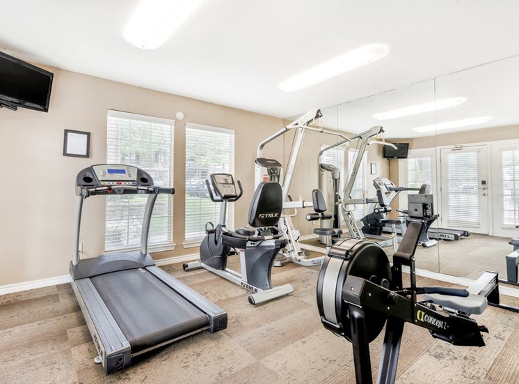 Fitness center with cardio machines, mounted tv on the left corner of room, and wall of mirrors.