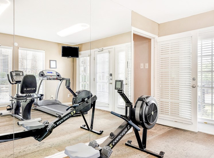 Fitness center with cardio machines, mounted tv on corner of room, and wall of mirrors.