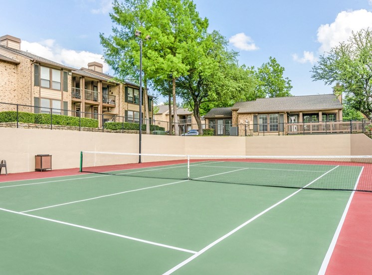 Fenced in tennis Court with trees and building exteriors in the background