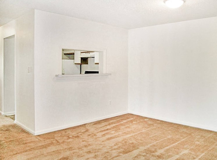 Carpeting dining area with white walls and view of kitchen in the background