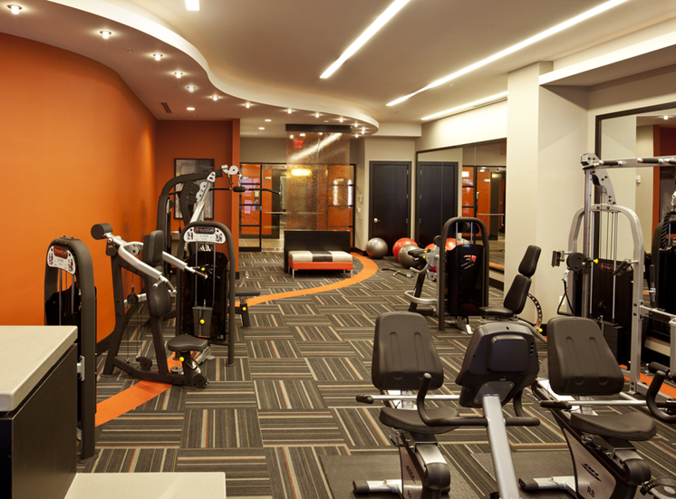 Fitness center with weighted equipment and full size mirrors against wall with orange accent colors
