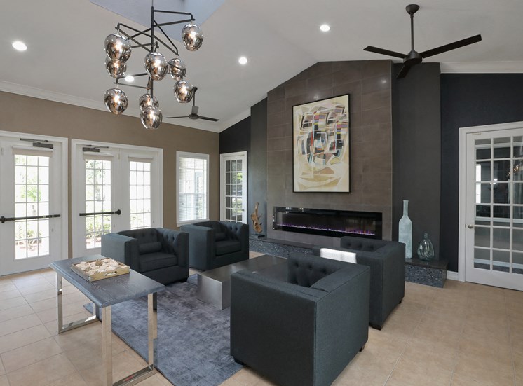 The Resident Lounge is a big room with a contemporary design. The far wall shows a large painting artwork above a fireplace. Four dark chairs are sat around a small table in front of french doors.