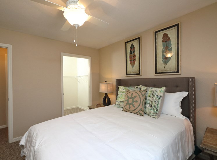 The Bedroom is a comfortable space with a large bed centered on the main wall. A large walk-in closet sits on the side of the room. The carpeted flooring continues throughout with furniture filling spaces around the room.