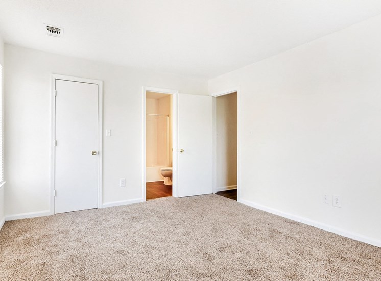 Carpeted bedroom with white walls and view of the bathroom and closet in the background Carpeted bedroom with white walls and view of the bathroom and closet in the background
