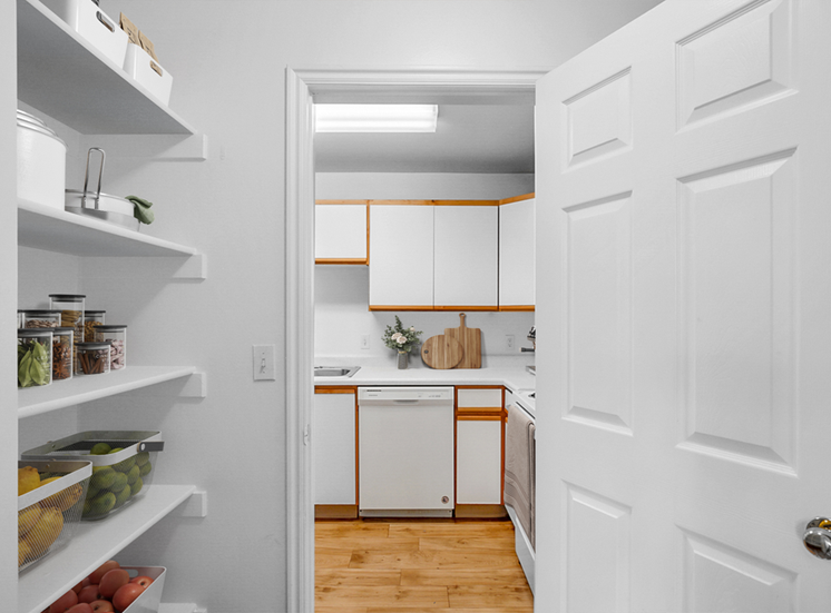 Virtually staged kitchen and pantry with white shelving, white cabinets, white appliances and wood floors