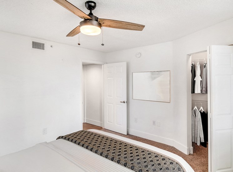 Model Bedroom with Bed Under Ceiling Fan, Nightstand Next to Open Walk In Closet