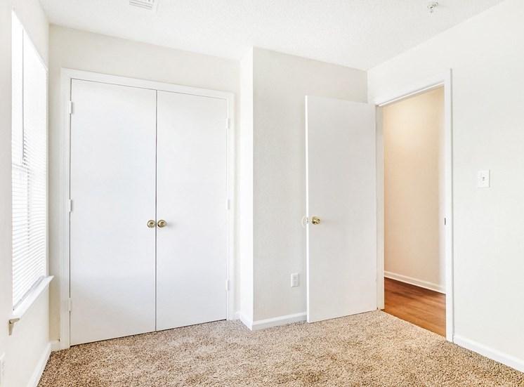 Carpeted bedroom with white walls and view of the hall and closet in the background