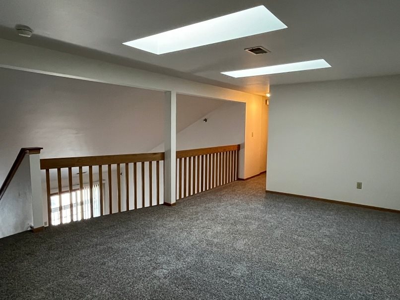 A room with a carpeted floor and a staircase with wooden railings.