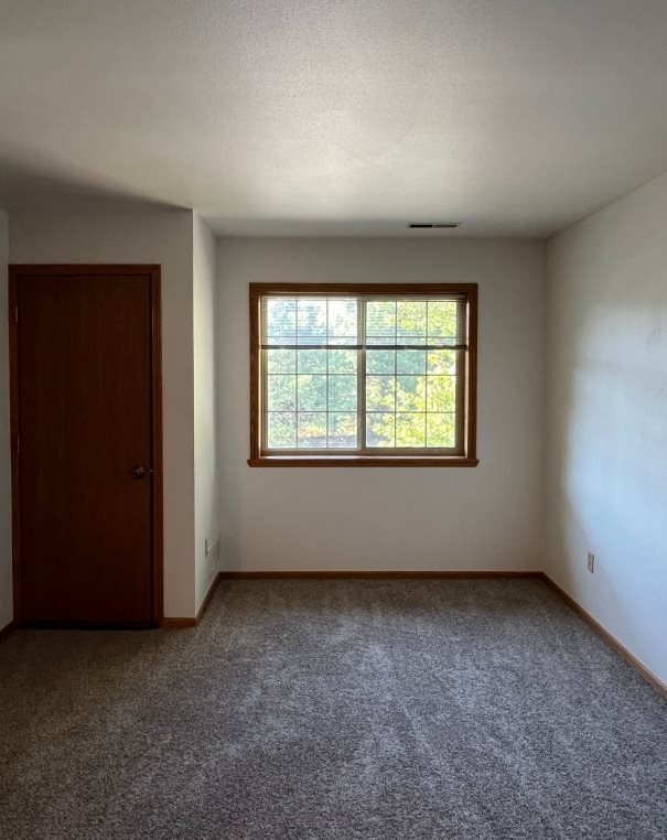 A room with a carpeted floor, a door, and a window with a view of a fence and trees.