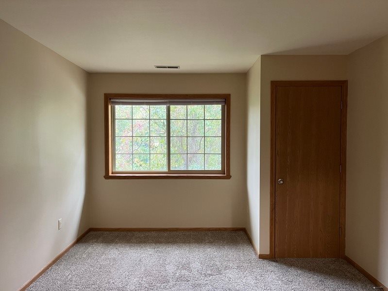 A room with a carpeted floor, a door, and a window with a view of trees outside.