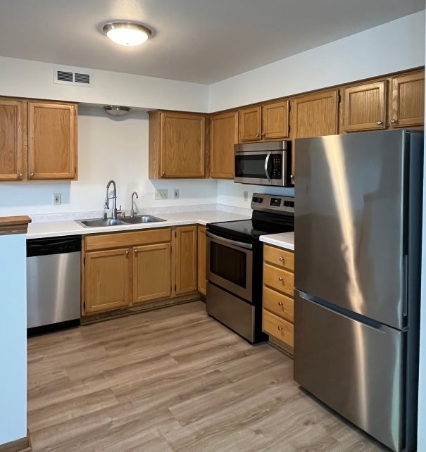 A kitchen with wooden cabinets and a stainless steel refrigerator.