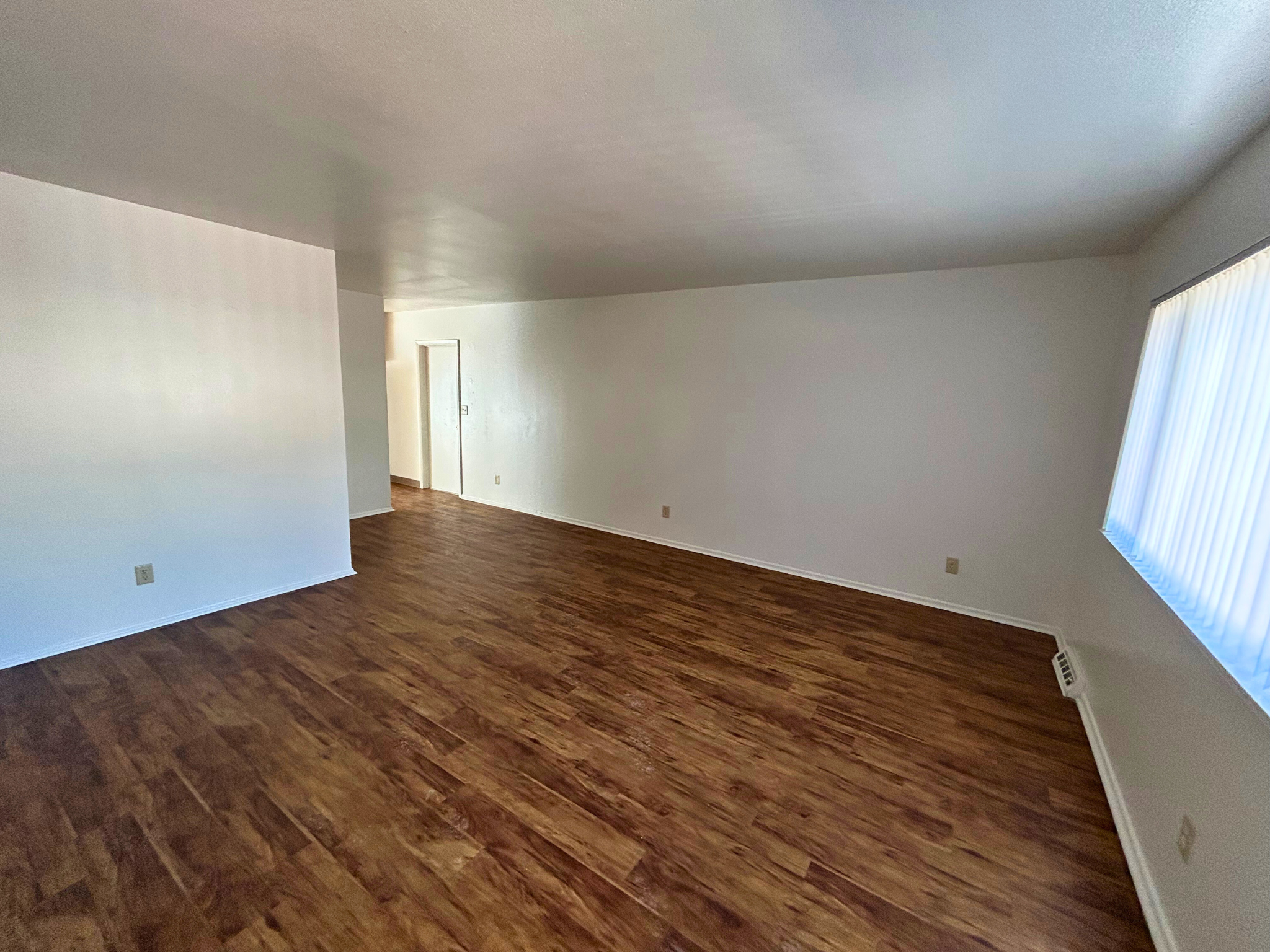 A room with wooden flooring and a door on the left side.