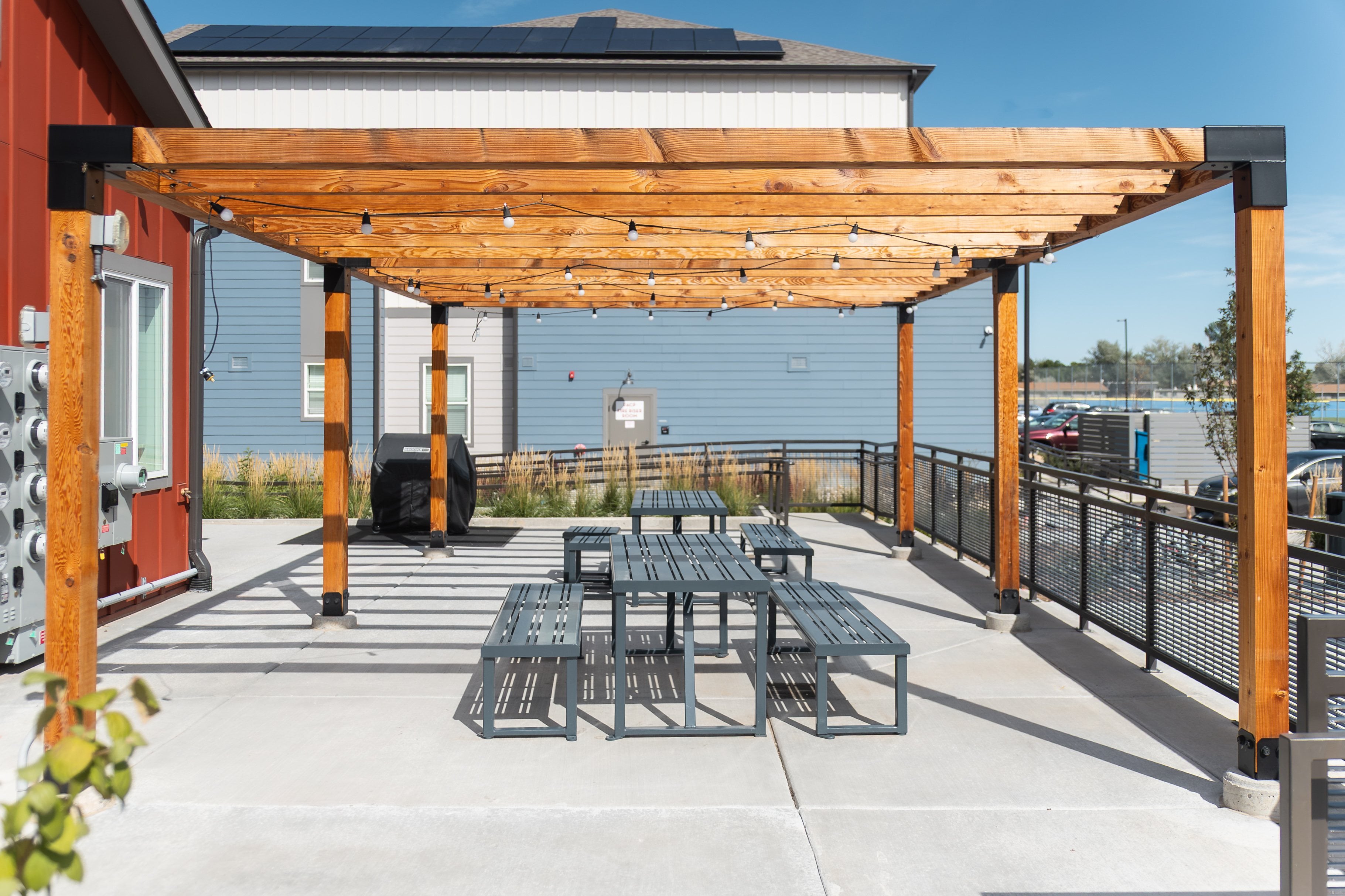 A wooden pergola with a table and chairs is in the foreground of the image.