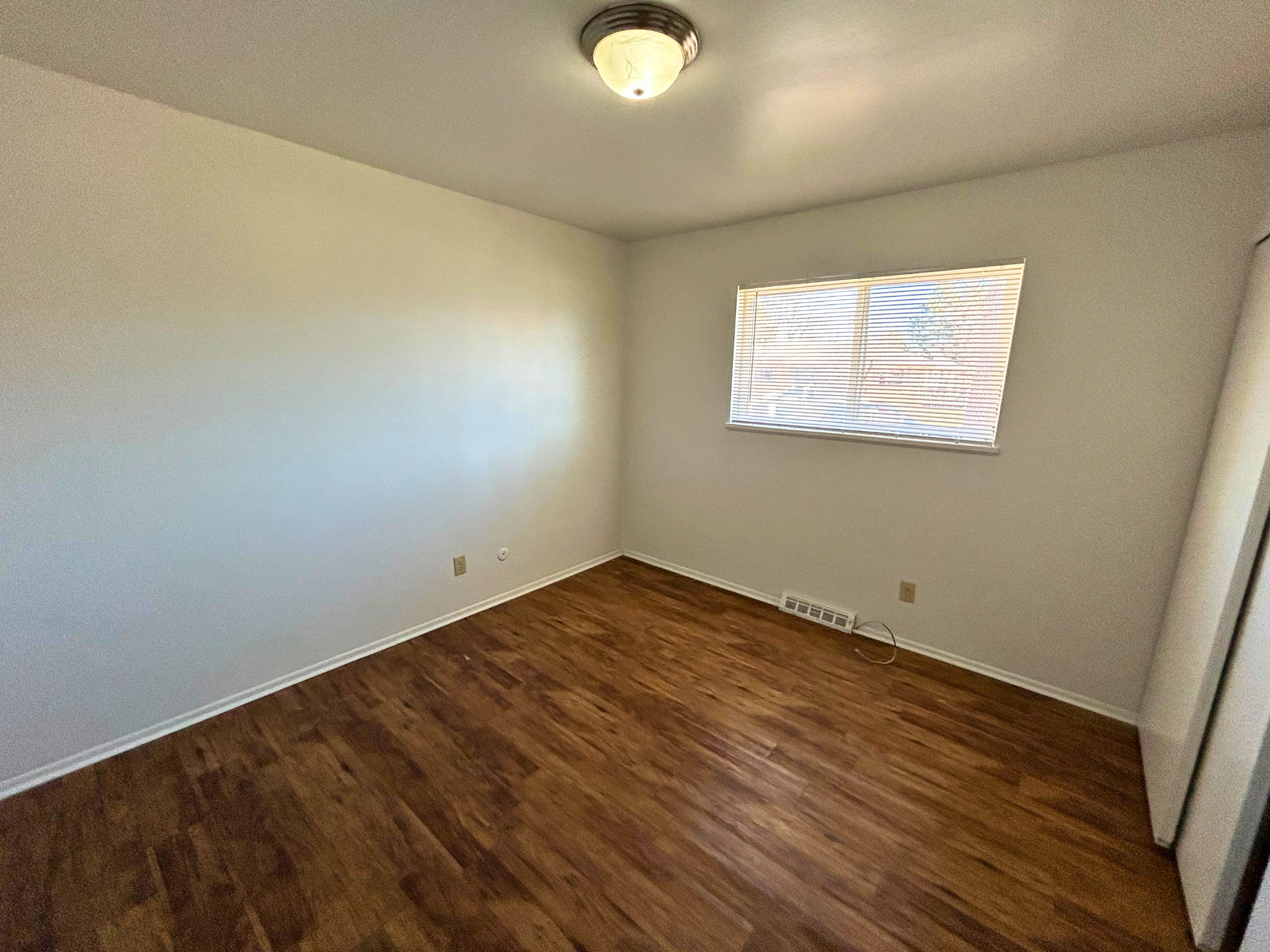 A room with wooden flooring and a window with blinds.