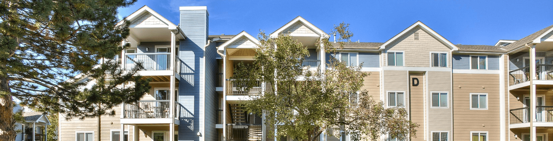 Apartment building with balconies and trees in front.