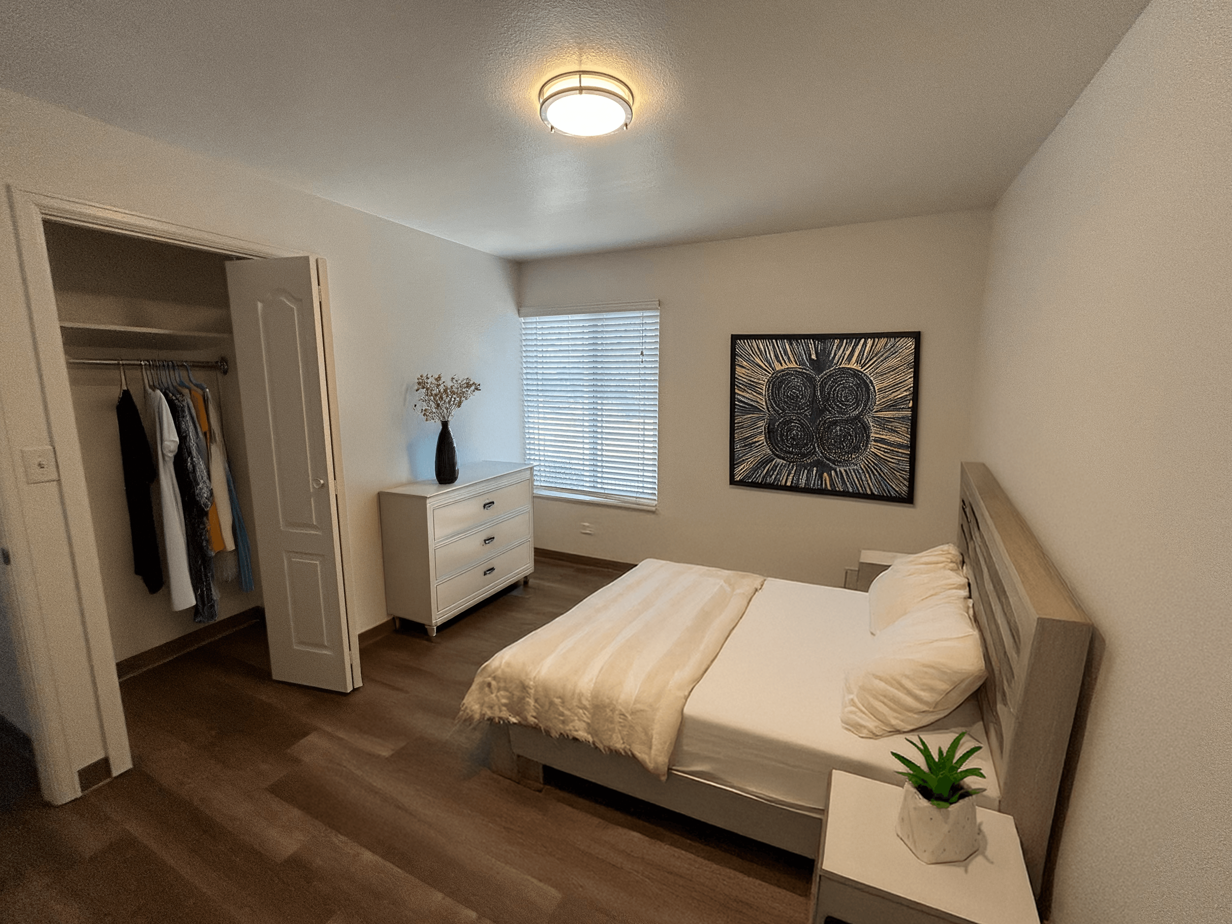 A bedroom with a bed, nightstand, and a dresser with clothes hanging on it.