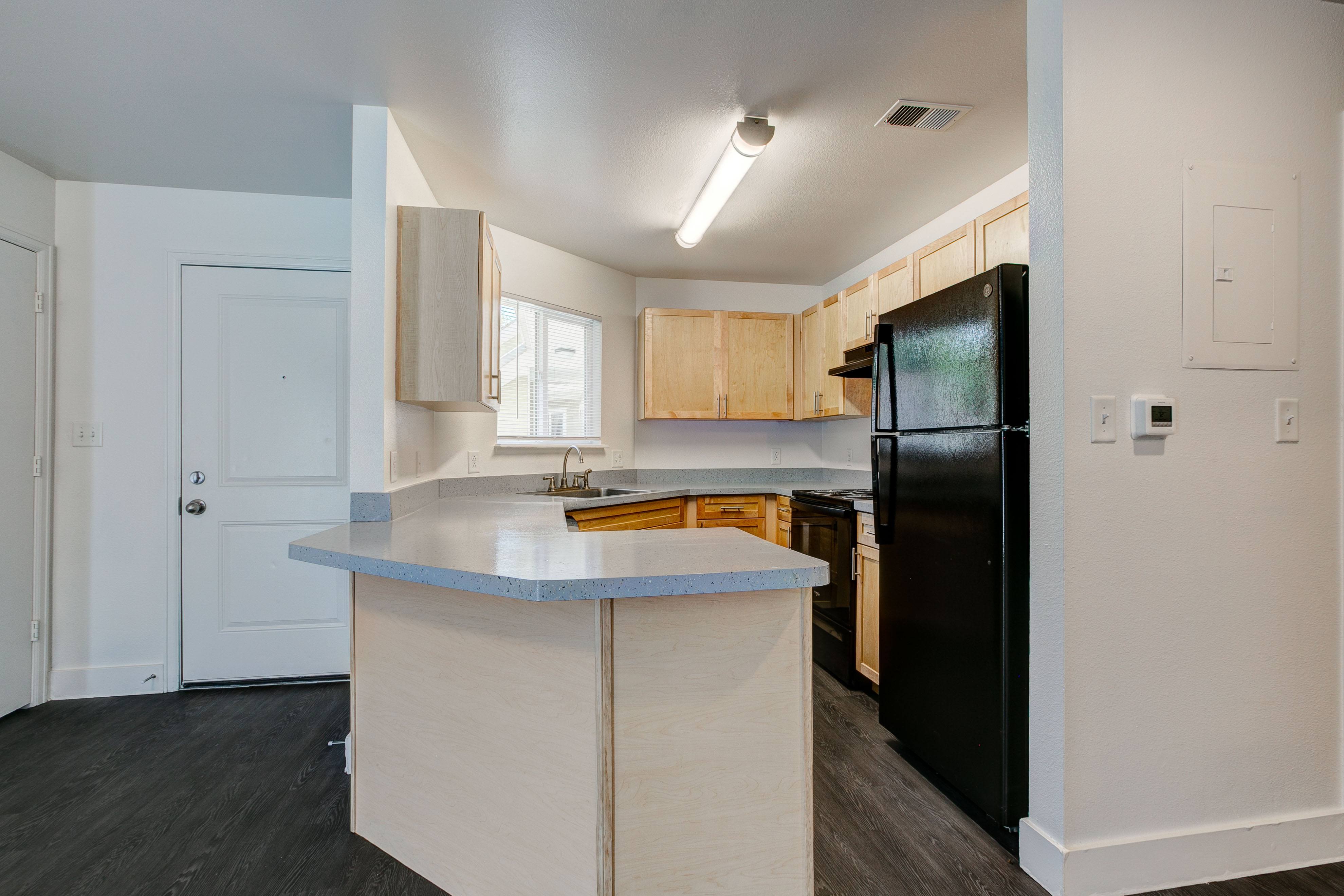 A kitchen with a black refrigerator and wooden cabinets.